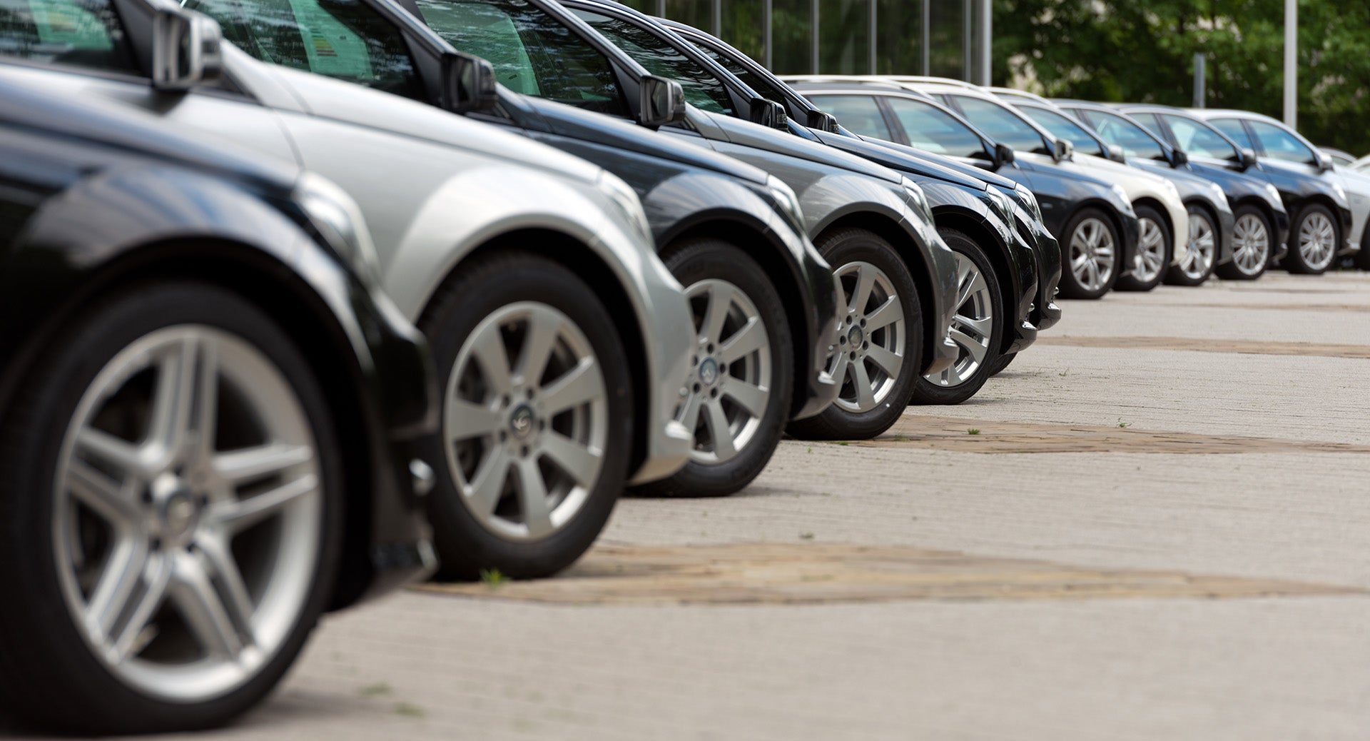 Row of parked cars at a dealership lot, lined up for sale.
